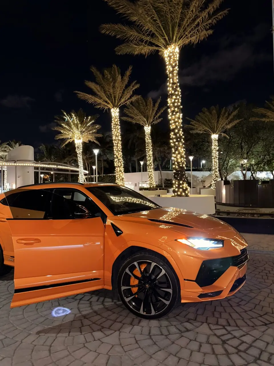 Pearl orange Lamborghini Urus S at night under palm lights