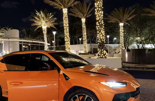 Pearl orange Lamborghini Urus S at night under palm lights